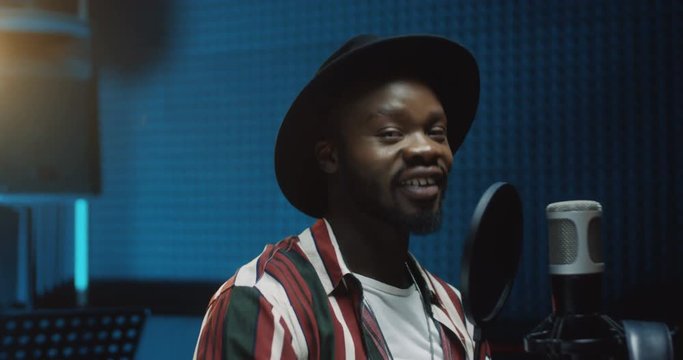 Close up of the young atractive and happy African American male singer taking off headphones and smiling to the camera after finishing recording a song in the sound studio. Portrait shot.