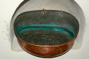 nostalgic and antique stoup with clear holy water, holy water in an old stoup made of copper with verdigris in the inside attached to a wall alcove in a church
