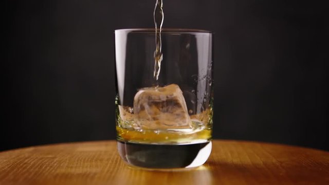 Delicious golden scotch whiskey being poured into glass by barman with perfect ice cube for a celebration drink