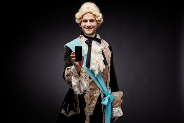 handsome victorian man in wig holding smartphone with blank screen on black