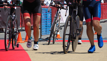 Group of people running with bicycles to transition area after cycling in triathlon championship - obrazy, fototapety, plakaty