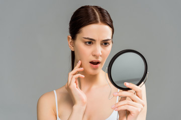 shocked young woman looking at mirror isolated on grey
