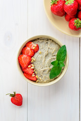 Hemp porridge with strawberries, mint and pine nuts. Vertical orientation, top angle, white wooden background.