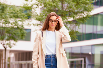 Fototapeta premium Smiling young businesswoman walking on the street near office buildings