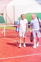 Full length of men in sports clothing talking while walking on tennis court during summer weekend