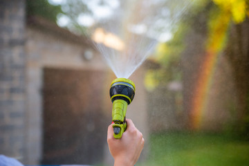 Woman's hand holding garden hose and spraying water to create rainbow. Rainbow in the background...