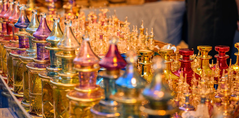 Close together standing richly decorated and colored perfume flacons made of glass in the light of the setting sun.