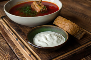 Borscht with sour cream on a wooden table.