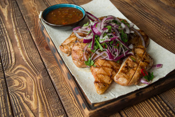 Grilled meat with onion and sauce on a wooden table.