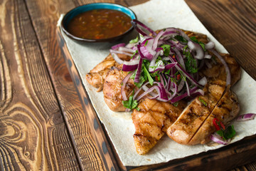 Grilled meat with onion and sauce on a wooden table.