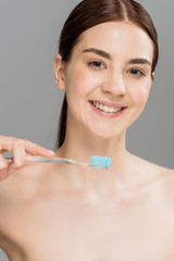 cheerful naked woman holding toothbrush while smiling isolated on grey
