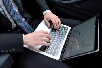View of hands of anonymous businessman, who is sitting in a car, with laptop and typing on keyboard.