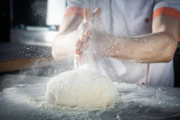 Chef prepares the dough with flour. male sprinkling flour over dough on table on dark background. horizontal. Copy space. Concept of flying food. Gluten free dough for pasta, bakery or pizza
