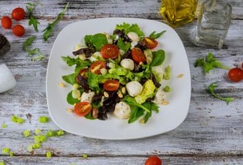 Fresh salad lettuce with mozzarella, tomatoes and olive oil wooden background.