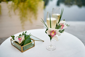 Sparkling wedding glasses with champagne, orchid flower decor and wedding rings in box in blur on...
