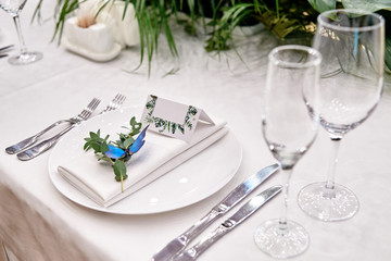 Table setting with blank guest card on empty white plate and cutlery on table, copy space. Menu mockup, place setting at wedding reception. Table served for wedding banquet in restauran