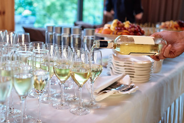 Waiter pours wine into wineglass at wedding reception, copy space. Sparkling glassware with wine and champagne on dinner table in restaurant