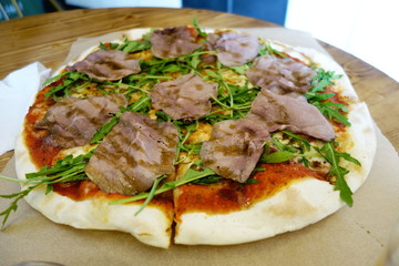 Pizza with slices of roast beef and rocket ruccola