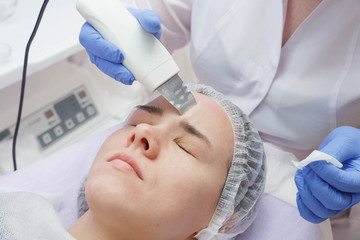 Naklejka premium The girl is provided with an ultrasound skin cleaning service in the beauty salon.