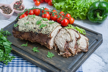 Baked pork chopped in a walnut and mint sauce on a cutting board with fresh herbs and vegetables. Light background.