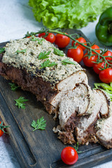 Baked pork chopped in a walnut and mint sauce on a cutting board with fresh herbs and vegetables. Light background.