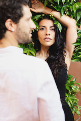 Street portrait of a woman on the background of a green leaves. In the foreground a blurred portrait of a man