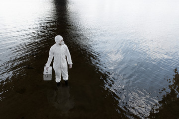 Overhead view of water inspector in protective costume holding inspection kit at river