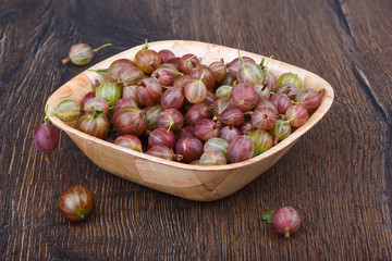 Ripe berries of a gooseberry in a wooden bowl on a wooden table.