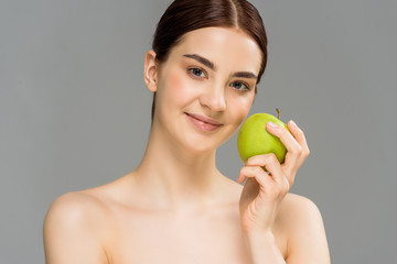 happy naked woman smiling while holding green apple isolated on grey