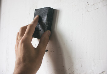 The worker grinds the wall with sandpaper
