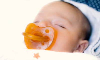 close-up rubber baby pacifier and sleeping baby on bed