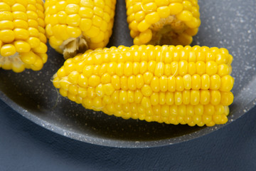 Fresh cooked yellow corn cobs lie on a gray dish