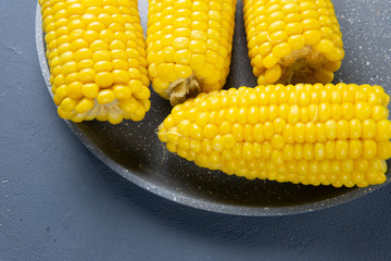 Fresh cooked yellow corn cobs lie on a gray dish
