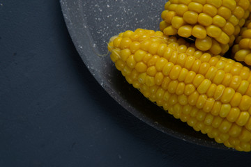 Fresh cooked yellow corn cobs lie on a gray dish