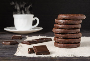 Chocolate cookies and pieces of chocolate on a dark table, in the background a Cup of hot coffee
