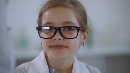 Portrait of a beautiful smart primary student girl with glasses smiling on camera having a science lesson in a laboratory.