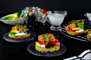 small canape with pink salmon fish, cucumber, tomato, olive and lemon on a black background. dark food photo