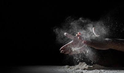 woman chef hand clap with splash of white flour and black background with copy space.