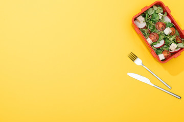 Fototapeta na wymiar top view of lunch box with salad near fork and knife