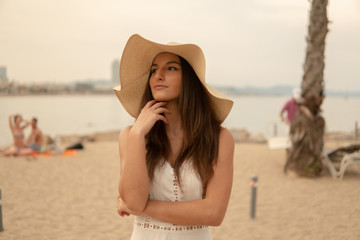 Pretty woman wearing white dress and pamela hat standing over the city beach, sea. Happy summer vacation