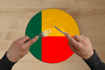 hands with cutlery on a plate with the state national flag of Benin, copy space