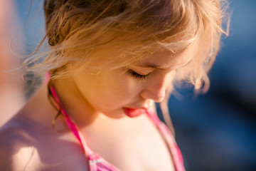 Portrait of a blonde girl with wet hair. Attractive child having fun on a tropical beach, playing with stones and water