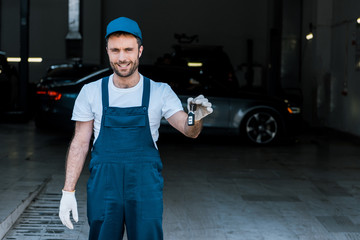 handsome bearded car mechanic holding keys in car service