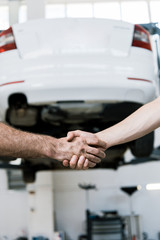 cropped view of auto mechanic shaking hands with man in garage