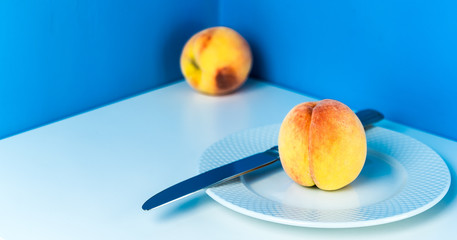 Ripe peach on a white plate with a knife on a blue background. Corner table