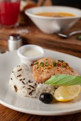 Steamed piece of salmon with boiled basmati rice in a white dish, served on a rustic wooden table