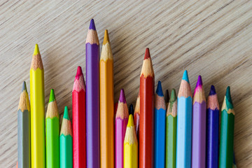 The group of a different length colored drawing pencils are laying on the wooden desk background and waiting for a painting lesson.