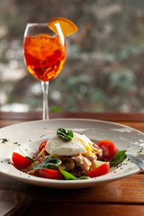 Salad with fresh vegetables, greens, crispy roasted bacon and poached egg with bitter Aperol Spritz on a terrace