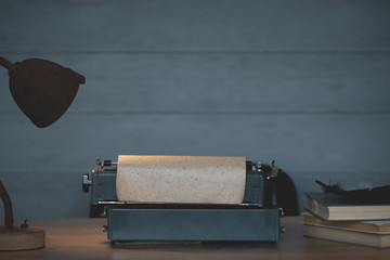 Old typewriter, books and lamp on a writer wooden desk background with copy space.