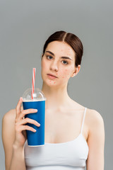 sad young woman with acne on face holding plastic cup isolated on grey